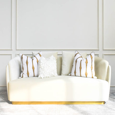 Sculptural cream velvet sofa with a double-curved back and gold-finished base, styled in a white and gold theme modern living room with throw cushions decor.