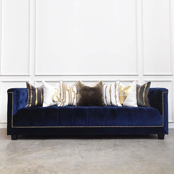 Fully fluffed cushions on top of Blue Chesterfield sofa with matching gold details. 