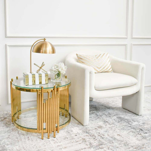This Canninghill Gold Glass Coffee Table inspired by Modern Art Deco pays homage to modern sculptures and arts. A touch of geometry plays up asymmetrical gold tubing details on the coffee table base. It sits luxuriously in this modern living room matched with a beautiful cream Chesterfield sofa and beautiful throw pillows.