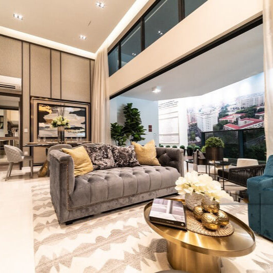 Shop the Esquire Chesterfield Sofa in grey. This image, from Singapore condo property developer, shows the tufted sofa styled in a high-ceiling luxury condo showflat living room with a gold coffee table, patterned rug, and elegant decor, demonstrating a luxurious living concept.
