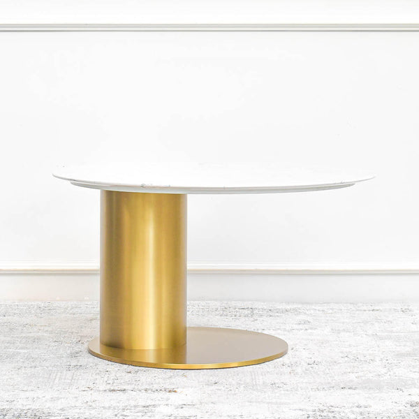 A gold plated stainless steel coffee table with a modern aesthetic, boasting a sculptured curved base and a white sintered stone tabletop, set against a white wall background.