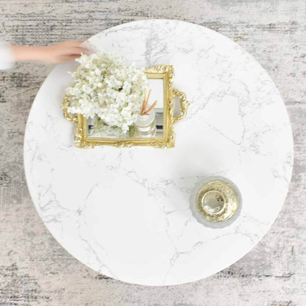 A white sintered stone tabletop, set on a luxury area rug, adorned with a vase of white flowers and a decorative tray.