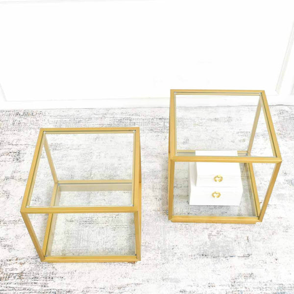 A pair of gold stainless steel square side tables with glass tabletops, positioned on a luxury area rug at Finn Avenue furniture showroom.