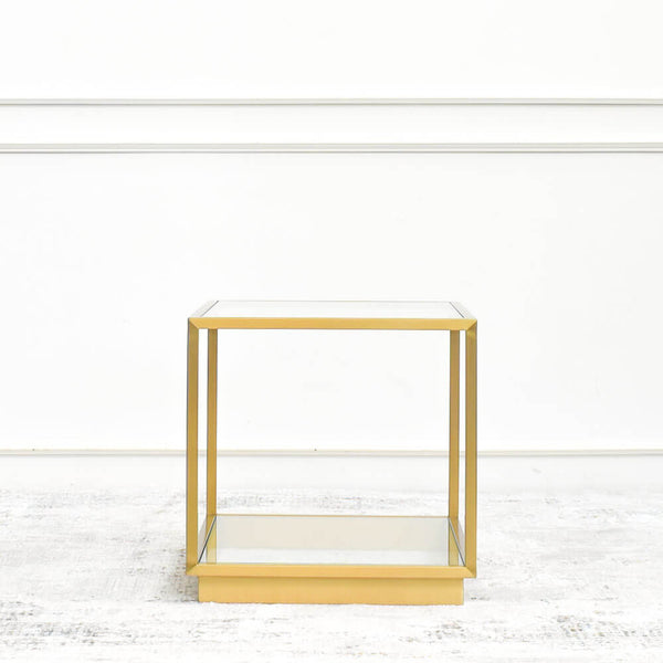 A gold stainless steel side table with a minimalist design, featuring a square frame and a glass tabletop, against a white background.