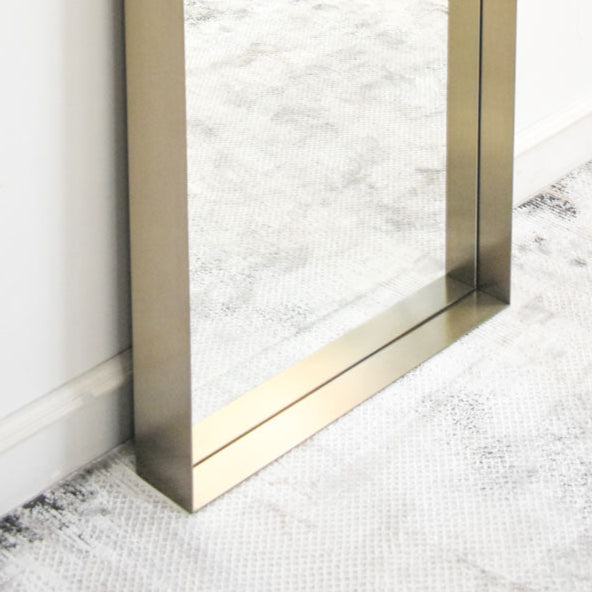 Elegant full-length mirror with a thin metallic frame in a sophisticated brass tone, leaned vertically on a white wall.