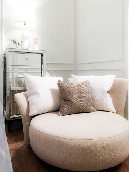 Luxury Paramour Round Sofa, custom upholstered in beige linen, in a reading nook, styled with a white table gourd lamp, flowers, and textured throw cushion.