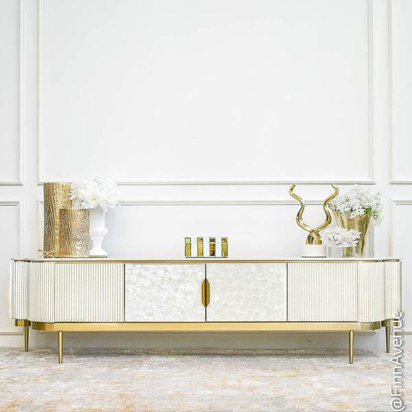 Perla 4-door white wood TV console featuring iridescent mother-of-pearl inlay doors and brushed gold stainless steel legs, styled in a spacious, timeless white and gold luxury living room.