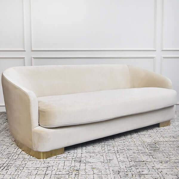 Curved 3-seater sofa in blush velvet with brushed gold base, styled in a modern living room.