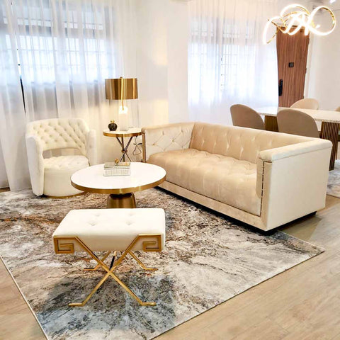 An Esquire Ivory Chesterfield Sofa from Finn Avenue, featuring deep button tufting and nailhead trim, takes center stage in a luxurious living room designed by Finn Avenue Stylists for an HDB flat in Singapore. The affordable luxury sofa is complemented by a Raphael Armchair, a Louis Coffee Table, a Marq Stool with a gold base, and a Curtis Rug, creating an elegant and comfortable space.