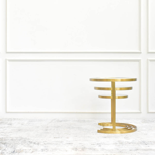 A set of three nesting side tables with circular tiers, stacked in ascending order of height, against a white wall with decorative paneling.