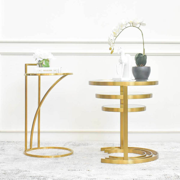 Two designs of slim side table and nesting coffee tables with multiple circular tiers, adorned with a white potted flower and a black potted plant, placed against a white wall on a luxury turkish area rug.