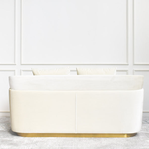 Zelda Ivory Curved Sofa with a gold base features its back profile. Ivory Cream velvet sofa sits luxurious on an area rug in neutral colour palette with a pop of gold at its bottom legs.