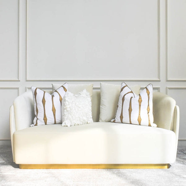 Zelda Ivory Curved Sofa with a gold base features Candice Olson Ivory White and Gold Throw Cushions as decor. It sits on luxurious area rug in neutral colour palette living room.