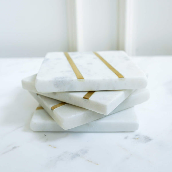 Stacked set of four natural white square marble coasters, brass inlaid stripes design.